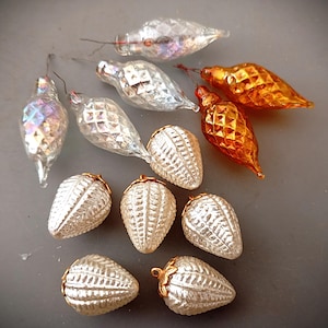 Op de afbeelding: Een verzameling vintage glazen ornamenten, waaronder vijf traanvormige stukken in heldere, iriserende en amberkleurige tinten met ruitvormige texturen, en vijf witte, getextureerde, aardbeivormige ornamenten met kleine goudkleurige metalen dopjes.