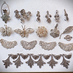 Könnte beinhalten: Eine Sammlung von silbernen Filigran-Schmuckkomponenten, darunter Schmetterlingsanhänger, Blumenbroschen und dekorative Blattformen. Die filigranen Designs zeigen filigrane Handwerkskunst, ideal für Basteln oder Schmuckherstellung.