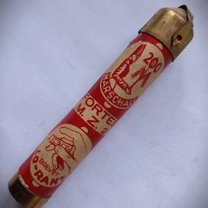 May include: A cylindrical red tube with metallic gold-toned caps on both ends. The label features the text MARSCHALL 200, FORTES M. Z. 2, and LO-RANT BREVET, along with a graphic illustration of a hand holding the object.