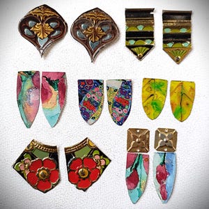 Könnte beinhalten: Eine Sammlung von Ohrringen im Vintage-Stil in verschiedenen Formen und Designs. Die Ohrringe weisen aufwendige Metallarbeiten, florale Muster und farbenfrohe Emaille-Details auf. Einige haben eine Tropfenform, andere sind quadratisch oder schildförmig.