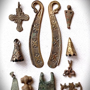 Könnte beinhalten: Eine Sammlung antiker Metallartefakte, darunter Anhänger, ein Kreuz und dekorative Stücke. Die Gegenstände haben verschiedene Formen und Größen, mit aufwendigen Designs und einem verwitterten Aussehen. Ein Messlineal aus Messing befindet sich im Hintergrund.
