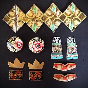 Könnte beinhalten: Eine Sammlung dekorativer Schmuckkomponenten und Verzierungen. Enthält florale runde Teile, rautenförmige Fliesen, kronenförmige Elemente und andere geometrische Designs. Die Teile weisen goldene, rote, grüne und blaue Akzente auf schwarzem Hintergrund auf.