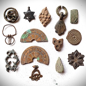 Könnte beinhalten: Eine Sammlung antiker Metallanhänger und -anhänger in verschiedenen Formen und Designs. Die Stücke umfassen einen Stern, einen sechszackigen Stern, einen Tropfen und eine Blume. Einige Stücke weisen komplizierte Muster und Texturen auf.
