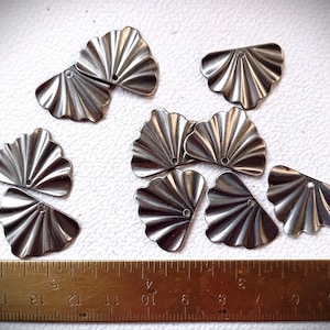 Puede incluir: Una colección de componentes metálicos plateados en forma de abanico, con un diseño acanalado y un pequeño agujero para la fijación. Una regla con medidas en centímetros se encuentra en la parte inferior de la imagen.