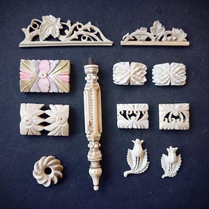 May include: A collection of off-white carved decorative elements including two long leaf-patterned strips, a central vertical spindle, two rectangular floral pieces with pink accents, four square floral tiles, a circular ring, and two small flower buds.