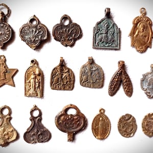 Può includere: Una collezione di ciondoli antichi in metallo di varie forme e design. I ciondoli sono in tonalità oro, bronzo e argento, con dettagli intricati e immagini religiose. Alcuni ciondoli presentano stelle, figure e motivi floreali.