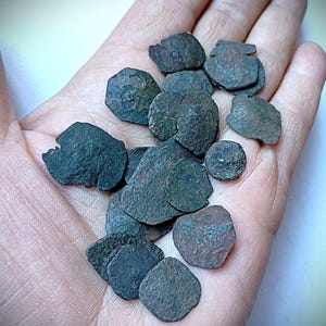 Könnte beinhalten: Eine Sammlung antiker Bronzemünzen in verschiedenen Formen und Größen. Die Münzen, gehalten in einer Hand, weisen Altersspuren auf und zeigen eine dunkelgrüne und braune Patina. Diese Münzen sind von historischem Interesse.