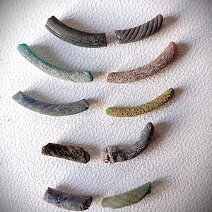 Puede incluir: Una variedad de objetos curvos y texturizados de varios colores. Los objetos incluyen tonos de verde, marrón y gris. Algunos tienen una apariencia lisa, mientras que otros tienen una textura acanalada o moteada. Están dispuestos sobre una superficie blanca y texturizada.