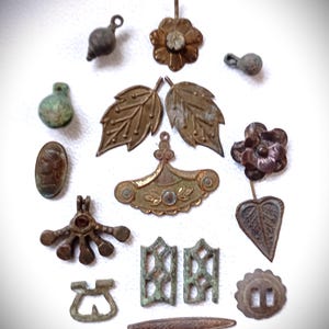 Könnte beinhalten: Eine Sammlung antiker Metallanhänger und -anhänger in verschiedenen Formen und Größen. Die Anhänger umfassen Blumen-, Blatt- und abstrakte Designs mit einer Farbpalette von Bronze bis Grünspan. Einige haben einen zentralen Stein oder Kristall.