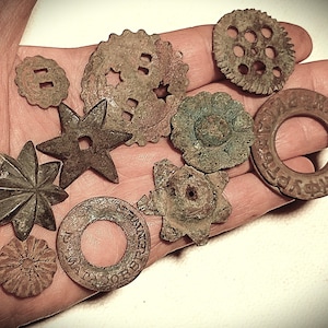 Könnte beinhalten: Eine Sammlung antiker Metallstücke in verschiedenen Formen, darunter Sterne, Zahnräder und florale Designs. Die Stücke weisen ein verwittertes, gealtertes Aussehen mit braunen und grünen Farbtönen auf, einige mit Text.