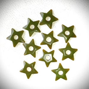 Op de afbeelding: Een verzameling olijfgroene, stervormige kralen met een centraal gat. De kralen hebben een glanzende afwerking en liggen verspreid op een witte ondergrond. Ideaal voor het maken van sieraden.