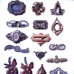 Könnte beinhalten: Eine Sammlung antiker bronzefarbener Metallschmuckteile, darunter verzierte Rahmen, dekorative Formen und ein Schleifenanhänger. Die Teile variieren in Größe und Design, mit komplizierten Details und gealterten Oberflächen. Ein Lineal befindet sich im Hintergrund.