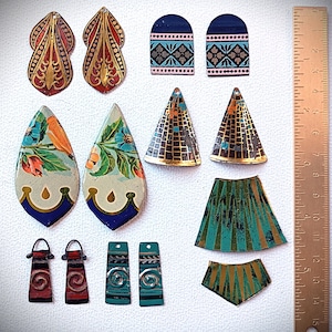 May include: A selection of colourful, vintage-style metal jewellery components. The pieces include earrings, pendants, and other decorative elements in various shapes, including teardrops, arches, and triangles. The designs feature floral patterns, geometric shapes, and metallic accents.