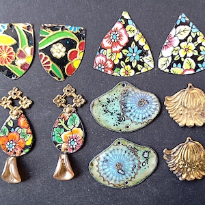 Könnte beinhalten: Eine Sammlung farbenfroher, dekorativer Metallanhänger und -charms. Die Anhänger zeigen florale Designs in Rot, Gelb und Blau auf schwarzem Hintergrund. Einige sind schildförmig, andere tropfenförmig, muschelförmig und dreieckig.