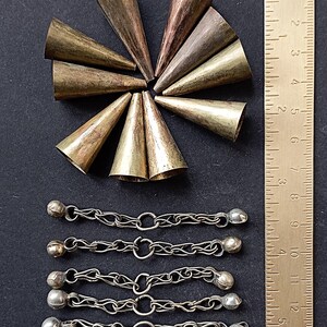 Op de afbeelding: Een assortiment metalen knutselbenodigdheden, waaronder kegelvormige kralen in brons en zilveren kettingaccenten met kleine belletjes. Een liniaal is inbegrepen voor de schaal. De kegels zijn ongeveer 2,5 cm hoog.