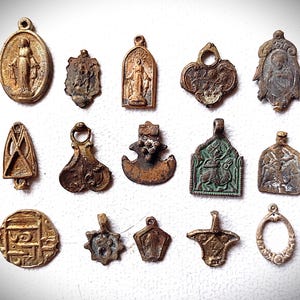 May include: A collection of antique metal pendants in various shapes and sizes. The pendants feature religious figures, floral designs, and abstract shapes. The colors range from bronze to dark brown, with signs of age and wear.