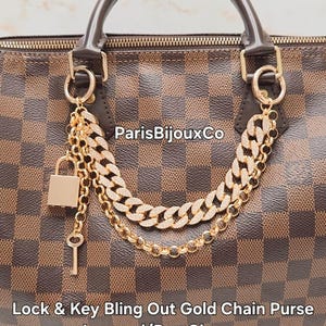 May include: A brown and tan checkered handbag with a gold chain and lock charm. The charm features a lock and key design. The text "ParisBijouxCo" is visible on the handbag.