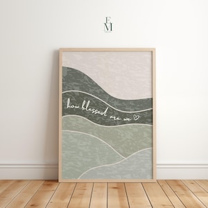 Könnte beinhalten: Ein gerahmter Kunstdruck mit einem minimalistischen Landschaftsdesign in Grün- und Beigetönen. Das Kunstwerk enthält den handgeschriebenen Text "how blessed are we" in weißer Schrift mit einem kleinen Herzsymbol. Der Rahmen ist hellholzfarben.