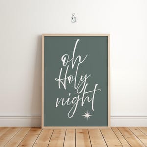 May include: A framed print with the words "oh Holy night" in white script on a dark green background. A white star is below the word "night". The frame is a light wood colour. The print is displayed on a wooden floor.