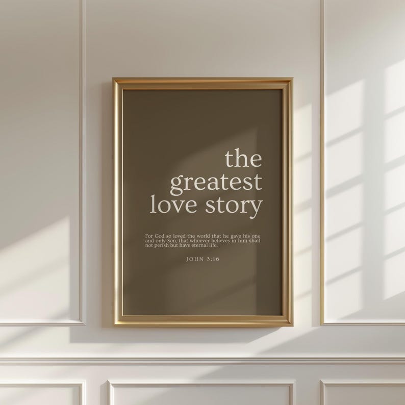 May include: A framed print with the text "the greatest love story" in white on a brown background. Below the title is a Bible verse from John 3:16. The frame is gold.