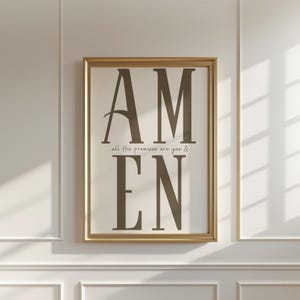 May include: A framed print with the word "AMEN" in large, dark brown letters. Below, smaller text reads "all His promises are yes &". The frame is gold, and the background is off-white.