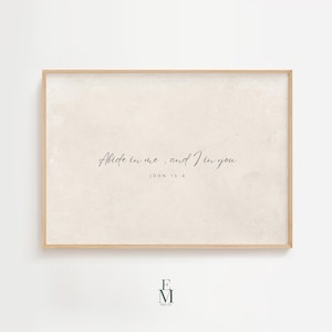 Op de afbeelding: Een ingelijste print met de tekst "Abide in me, and I in you. John 15:4" in een sierlijk handschrift. De achtergrond is een zachte, neutrale tint en de lijst is van licht hout. De print heeft een minimalistisch ontwerp.