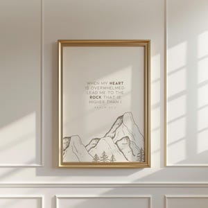 May include: A framed print with a gold-colored frame. The print features a mountain illustration in black and white, with the text "WHEN MY HEART IS OVERWHELMED. LEAD ME TO THE ROCK THAT IS HIGHER THAN I. PSALM 61:2."