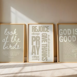May include: Three framed art prints with gold frames. The prints feature inspirational quotes in white text on a light gray background. The quotes include "look at the birds", "Rejoice always, pray without ceasing, give thanks", and "God is Good".