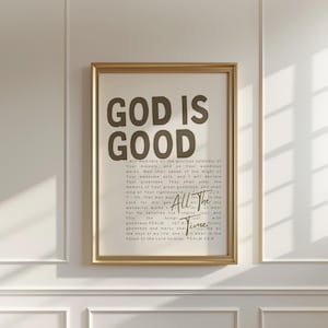 May include: A framed print with the words "GOD IS GOOD" in large, bold letters at the top. Below, smaller text includes a Bible verse. The frame is gold, and the background is a neutral color.