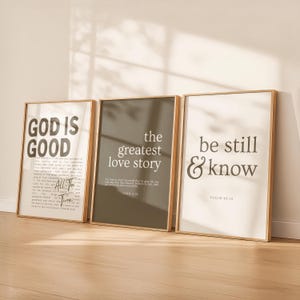 May include: Three framed art prints with inspirational quotes. The first reads "GOD IS GOOD", the second "the greatest love story", and the third "be still & know". Each print has a white or dark background with gold frames.