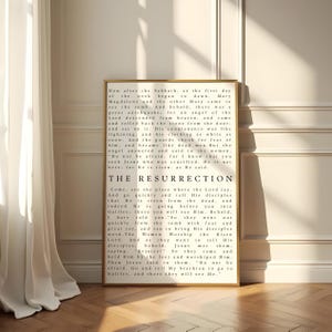 May include: A framed print featuring the text "The Resurrection" in black on a white background. The print has a gold frame. The text is a passage from the Bible. The print is displayed on a wooden floor.