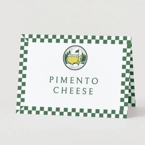 May include: A white card with a green and white chequered border. The card has a green logo with a yellow golf course and the text "Masters" in the centre. The text "Pimento Cheese" is printed in black below the logo.