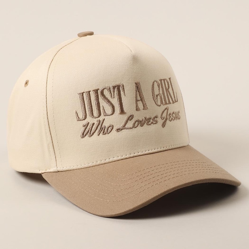 May include: A beige and brown baseball cap with the embroidered text "JUST A GIRL Who Loves Jesus". The cap has a curved brim and a button on top. The hat is made of a durable fabric.