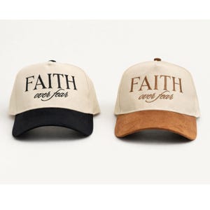 May include: Two baseball caps with the text "FAITH over fear". One cap has a black brim, the other has a brown brim. Both caps have a cream-colored crown.
