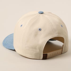 May include: A beige baseball cap with a light blue brim and button. The cap has a curved brim and an adjustable strap at the back. The cap is made of a durable fabric.