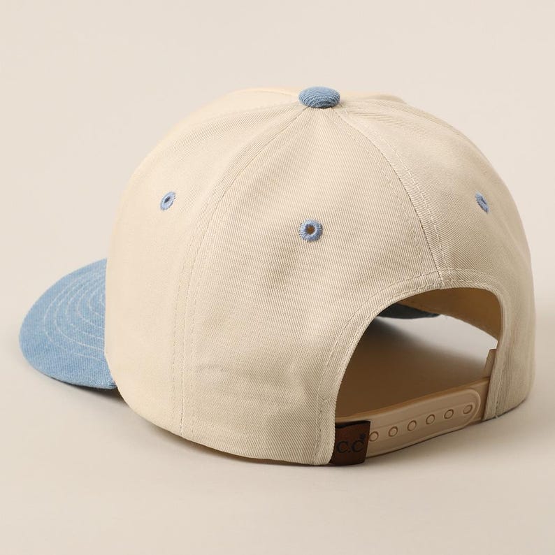 May include: A beige baseball cap with a light blue brim and button. The cap has a curved brim and an adjustable strap at the back. The cap is made of a durable fabric.
