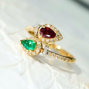 Könnte beinhalten: Ein goldener Ring mit einem birnenförmigen Smaragd und Rubin, die in einem Halo aus Diamanten gefasst sind. Der Ring ist so konzipiert, dass er am Knöchel getragen werden kann.