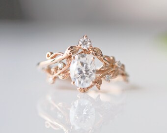 May include: A rose gold engagement ring with a large oval-shaped diamond surrounded by delicate leaf and vine details. Smaller diamonds are set in the leaves.