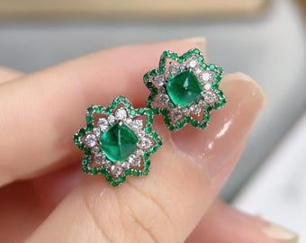 May include: A pair of emerald green and white gemstone earrings. Each earring features a square-cut, vibrant green center stone surrounded by a floral design of smaller green and white gemstones. The earrings are set in a silver or white metal.