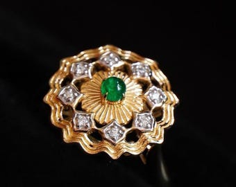 May include: A gold ring with a floral design. A round, green gemstone is at the centre, surrounded by gold rays. The outer ring has diamond-like stones set in a geometric pattern. The ring is set against a black background.