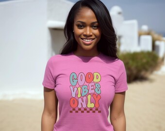 May include: A pink t-shirt with the text "GOOD VIBES ONLY" in colorful, bubble-like letters. The text is outlined in black and has a checkered pattern underneath.