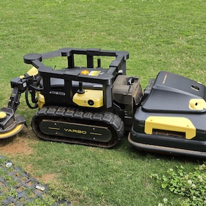 Peut inclure: Un système d'entretien de pelouse robotisé Yarbo noir et jaune sur une pelouse herbeuse. Le système comprend une base chenillée, une unité de tonte et un bras avec une tête de coupe circulaire. Le système est conçu pour la tonte automatique.