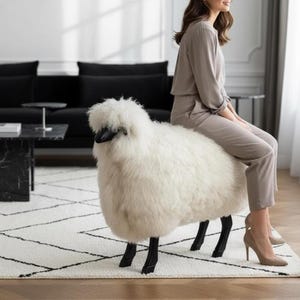 May include: A white sheep-shaped ottoman with black legs and a black head. The ottoman is placed on a white rug with a black geometric pattern. A person is sitting on the ottoman in a room with a black sofa and marble coffee table.