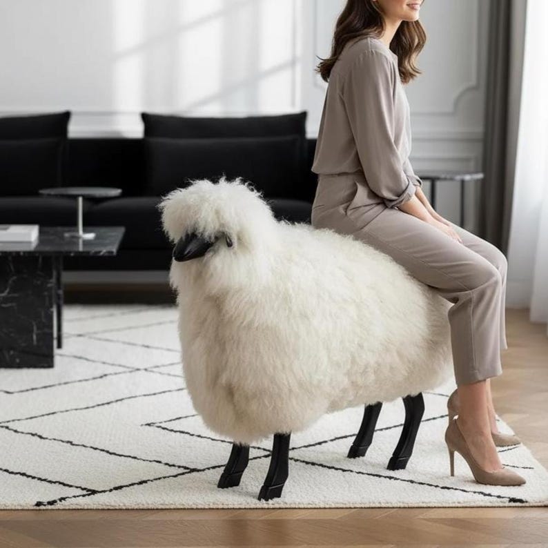 May include: A white sheep-shaped ottoman with black legs and a black head. The ottoman is placed on a white rug with a black geometric pattern. A person is sitting on the ottoman in a room with a black sofa and marble coffee table.