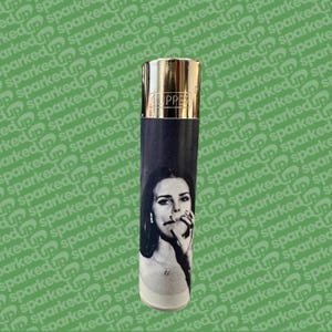 May include: A black and white Clipper lighter featuring a woman with a cigarette. The lighter has a gold-coloured top and the word "CLIPPER" is printed on the top. The lighter is cylindrical in shape.