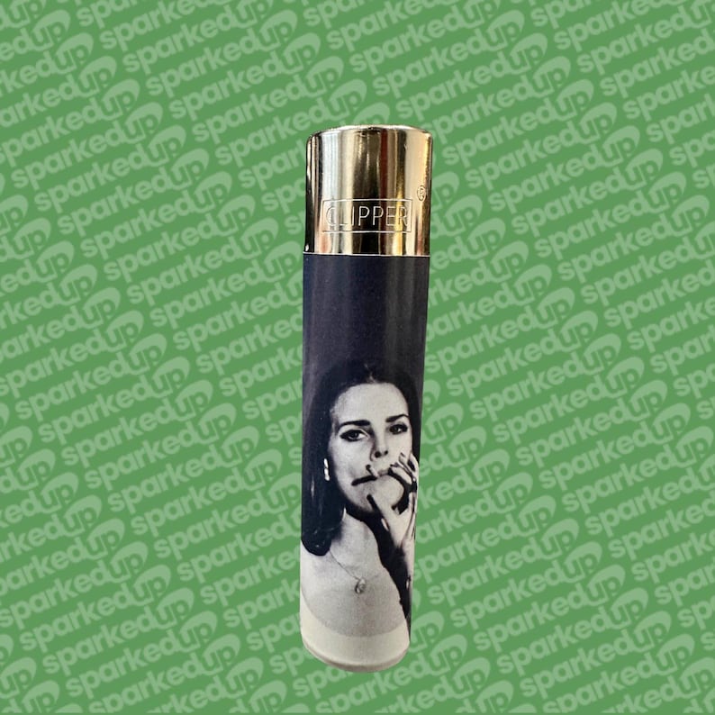 May include: A black and white Clipper lighter featuring a woman with a cigarette. The lighter has a gold-coloured top and the word "CLIPPER" is printed on the top. The lighter is cylindrical in shape.