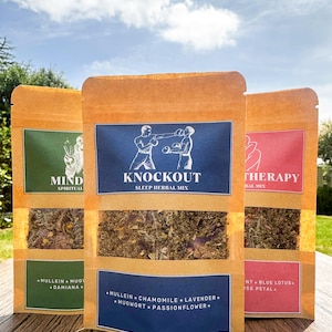 Pode incluir: Três sacos de papel castanho com janelas transparentes, cada um contendo misturas de ervas. O saco central tem um rótulo azul com uma ilustração de boxe e o texto "KNOCKOUT SLEEP HERBAL MIX". Os outros sacos têm rótulos verdes e vermelhos.