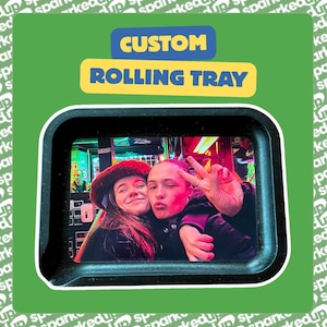 May include: A black rectangular rolling tray featuring a custom photographic insert of two individuals posing together. The text "CUSTOM ROLLING TRAY" is printed in blue and yellow above the tray against a green background with repeating text.