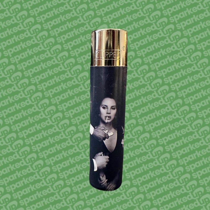 May include: A black and gold Clipper lighter. The lighter has a black and white image of a woman holding a cigarette. The top of the lighter is gold metal, with the word "CLIPPER" printed on it.