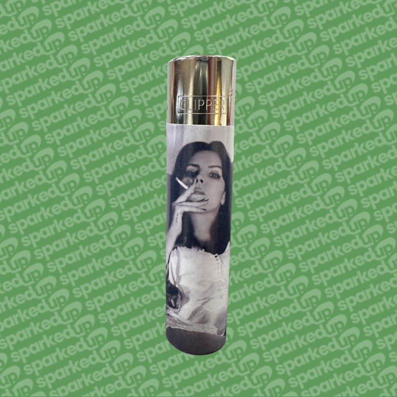 May include: A silver Clipper lighter featuring a black and white portrait of a woman smoking. The lighter has a metallic top and a black base. The image is printed on a paper sleeve wrapped around the lighter.